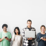 Eine Gruppe von sieben Menschen steht nebeneinander vor einer weißen Wand, alle konzentriert auf ihre digitalen Geräte. Die Personen sind vielfältig in Alter, Geschlecht und Stil, einige lächeln, andere sind vertieft in ihre Smartphones, Tablets oder Laptops.